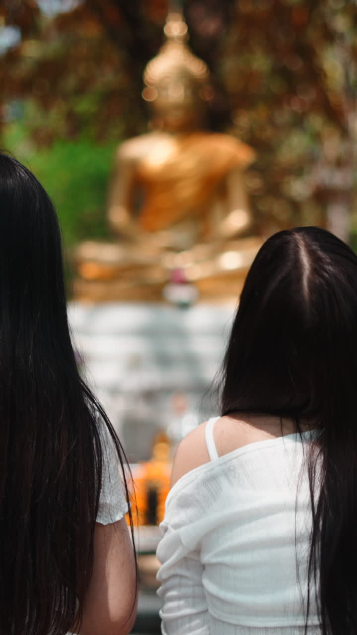 Duas mulheres observando uma estátua dourada de Buda em um jardim de templo