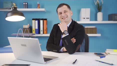 hombre de negocios mirando a la cámara y sonriendo mientras trabaja en la computadora portátil.