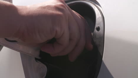 close up of a woman's hand tightening the cap on the gas tank of a white vehicle