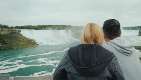 active married couple spends a weekend at niagara falls looking into the distance at the cascade of