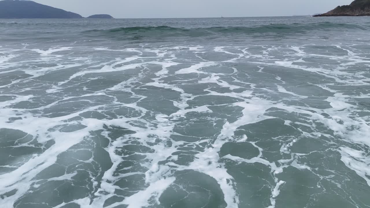 Beelden op grondniveau van oceaangolven, met schuimende branding, waterbeweging en kustlandschap. Perfect voor cinematografische, reis- of natuurthema-projecten