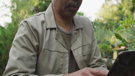 jardinero afroamericano usando una tableta en el centro de jardinería, mirando a la cámara y sonriendo
