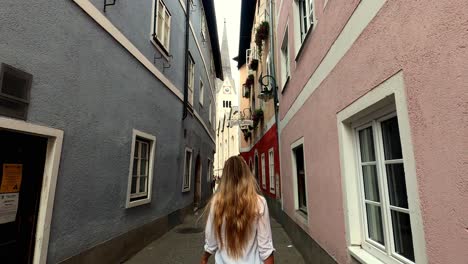 una chica blanca con el pelo largo y rubio camina por un viejo y estrecho callejón europeo hacia una iglesia en un pequeño pueblo austriaco