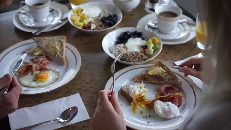 hombre y mujer tomando tocino y huevo, muesli casero, café y jugo de naranja para desayunar en un hotel de lujo