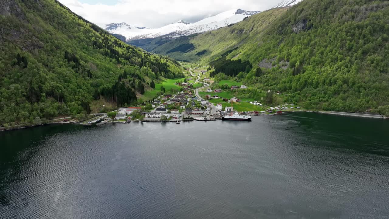 concepto de infraestructura rural de noruega - el ferry está junto a la pequeña ciudad de eidsdal - aérea moviéndose hacia el ferry y el pueblo con laderas verdes y fondo de montañas cubiertas de nieve