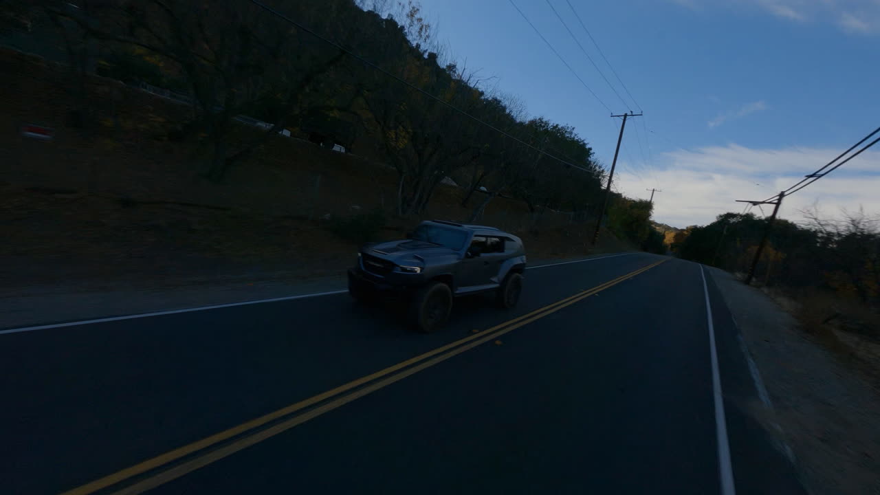 Vista drone FPV di un'auto nera che guida velocemente su strada al mattino.