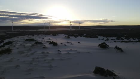 Drone-Aéreo-Sobre-Dunas-De-Arena-Alejándose-Mostrando-Molinos-De-Viento-Durante-El-Amanecer