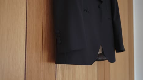 stylish black suit jacket hanging on warm wooden wall
