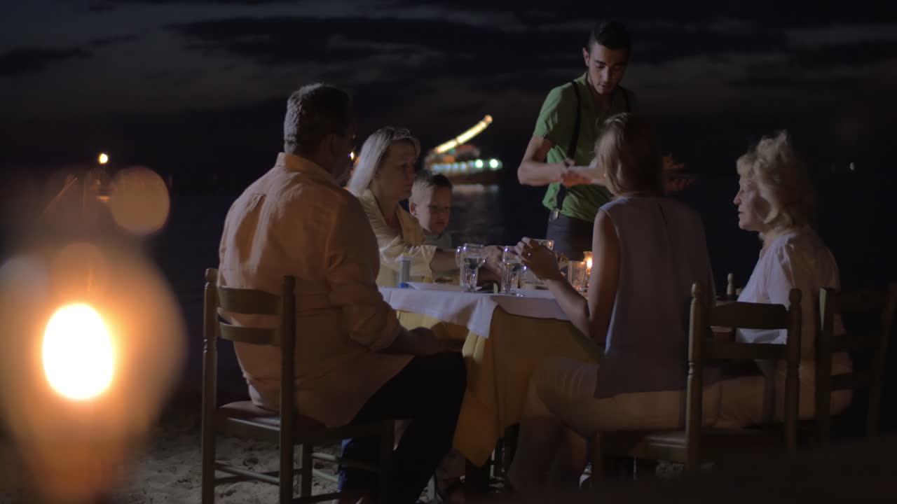 официант, подающий ужин семье в открытом кафе