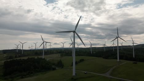 gray clouds over rows of wind turbines generating renewable energy on the vast field in quebec, canada at dusk - aerial drone, pullback shot