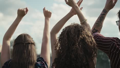 Rear-view-of-friends-dancing-on-music-festival-with-hands-up.