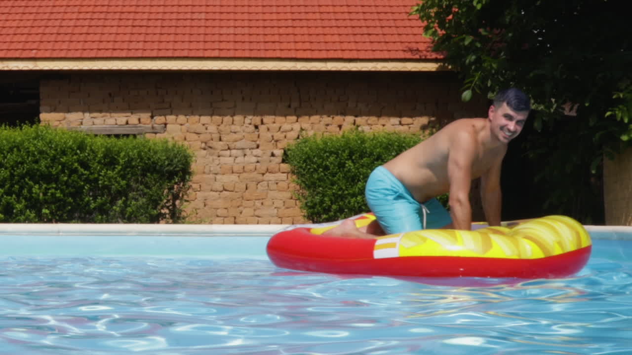 hombre equilibrando en un flotador de piscina colorido, día de verano por una casa rústica