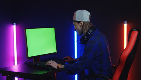 junger mann, der auf dem computer mit chroma-key-bildschirm spielt, schaut dann auf die kamera und lächelt