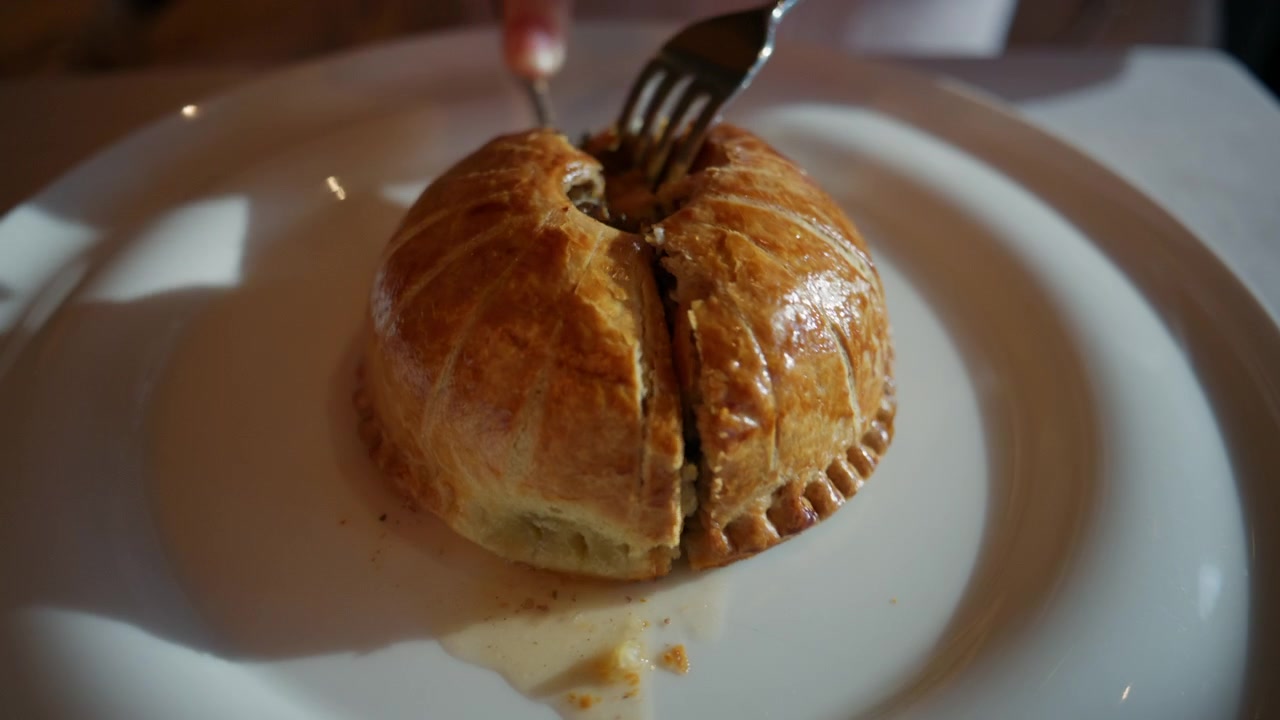 Primo piano di un Beef Wellington gourmet che viene affettato su un elegante piatto da ristorante.