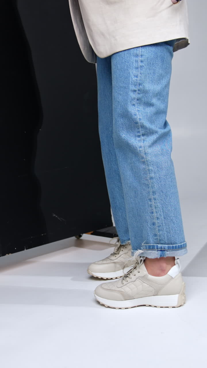 Unrecognized female wearing jeans and jacket holding a bag. Model in sports shoes standing near the black screen. Vertical video