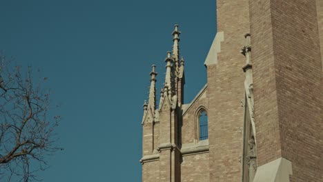 close up of gothic church spires against a clear blue sky, with bare branches in the frame