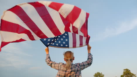 woman running with american flag in her hands flag waving against sky background rear view