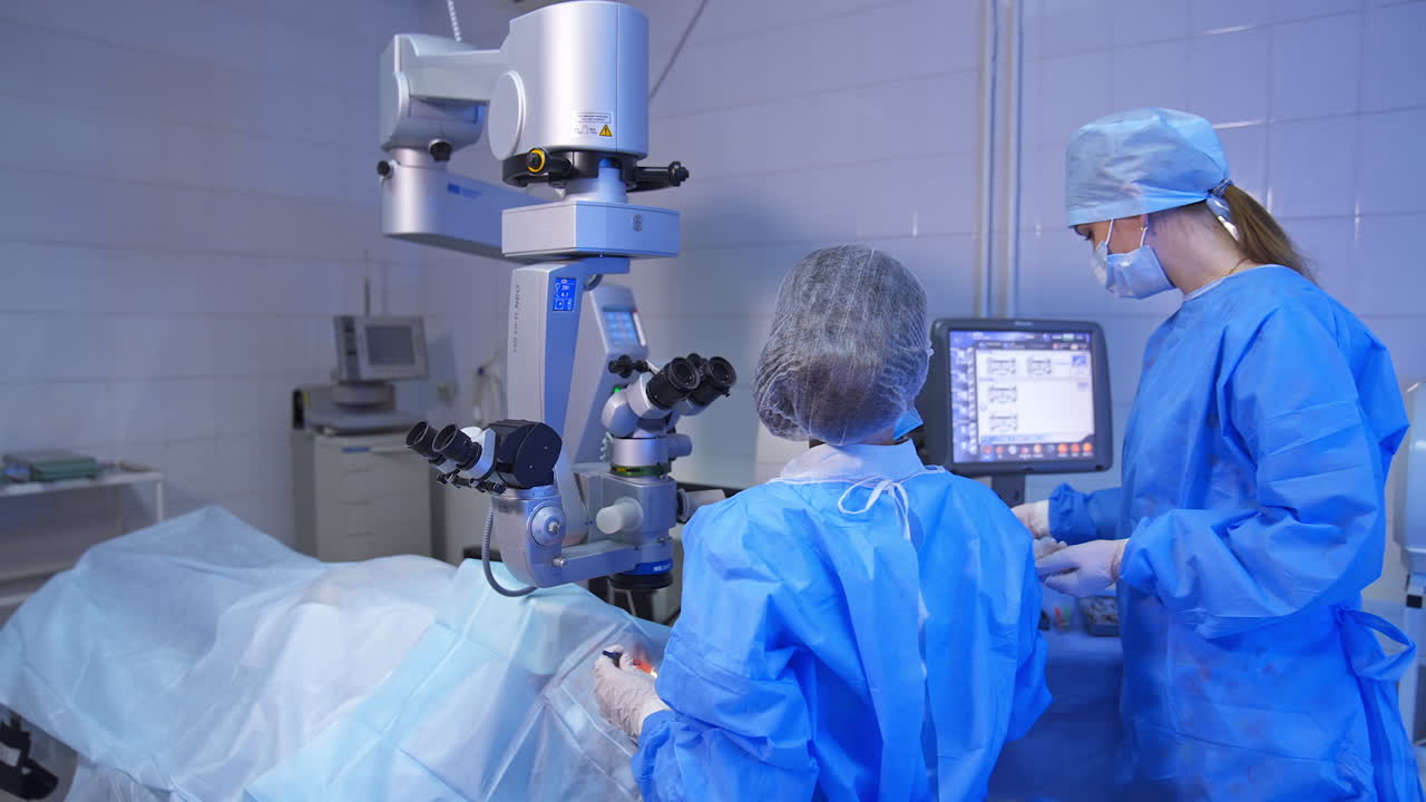 Ophthalmologist performing eye operation. Female assistant standing beside near the table with tools and equipment.