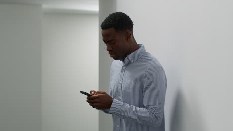 young businessman in office looking at message with bad news on mobile phone and leans against wall looking unhappy and depressed 4