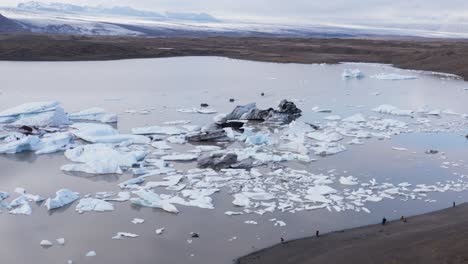 adventure boat tour in glacial lake with icebergs, tourist people on shore enjoying wild cold landscape, aerial