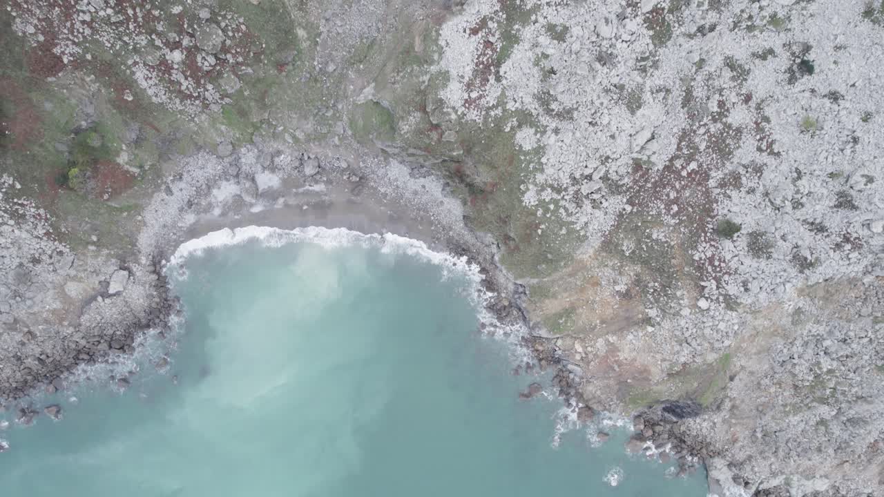 Foamy turquoise sea washing shore surrounded by rocky cliff. Cantabria, Spain