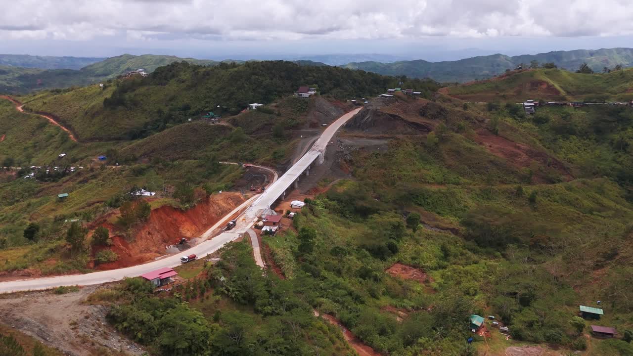 Panoramic 4K aerial drone shot of a long concrete bridge viaduct connecting steep mountain ridges. Major infrastructure development project in a rural landscape with exposed red soil