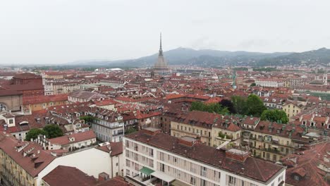 Colorful-rooftops-of-Turin-with-Mole-Antonelliana-building-in-front,-aerial-ascend-view