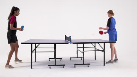 competing in table tennis match indoors, two women playing intensely
