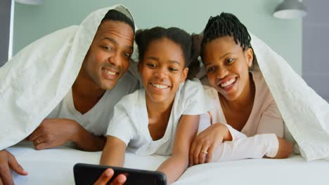 Front-view-of-happy-black-family-taking-selfie-with-mobile-phone-on-bed-in-a-comfortable-home-4k