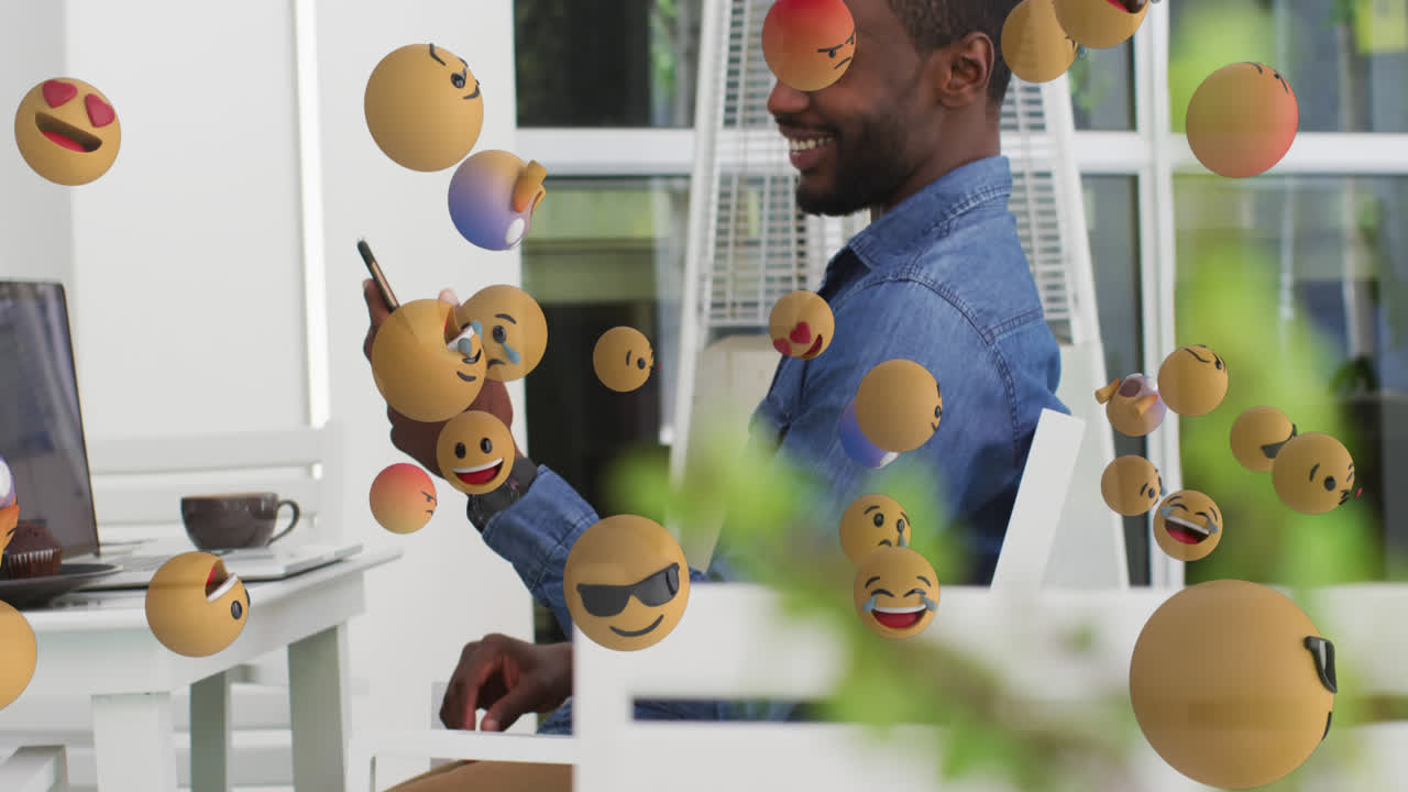 múltiples emojis faciales flotando contra un hombre afroamericano que usa un teléfono inteligente