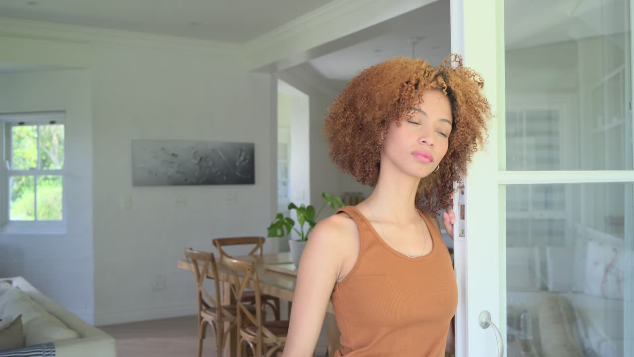 Mulher afro-americana de regata em casa, vendo a luz se mover enquanto olha pela porta de correr, com espaço para texto.