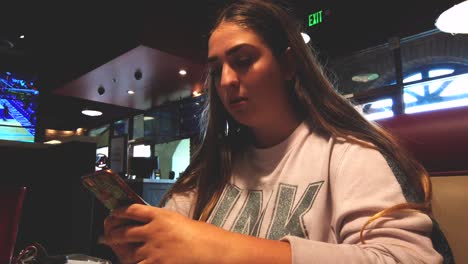 Static-shot,-of-teenage-female-on-phone,-in-restaurant,-looking-at-social-media-and-texting,-at-lunch,-in-California,-USA