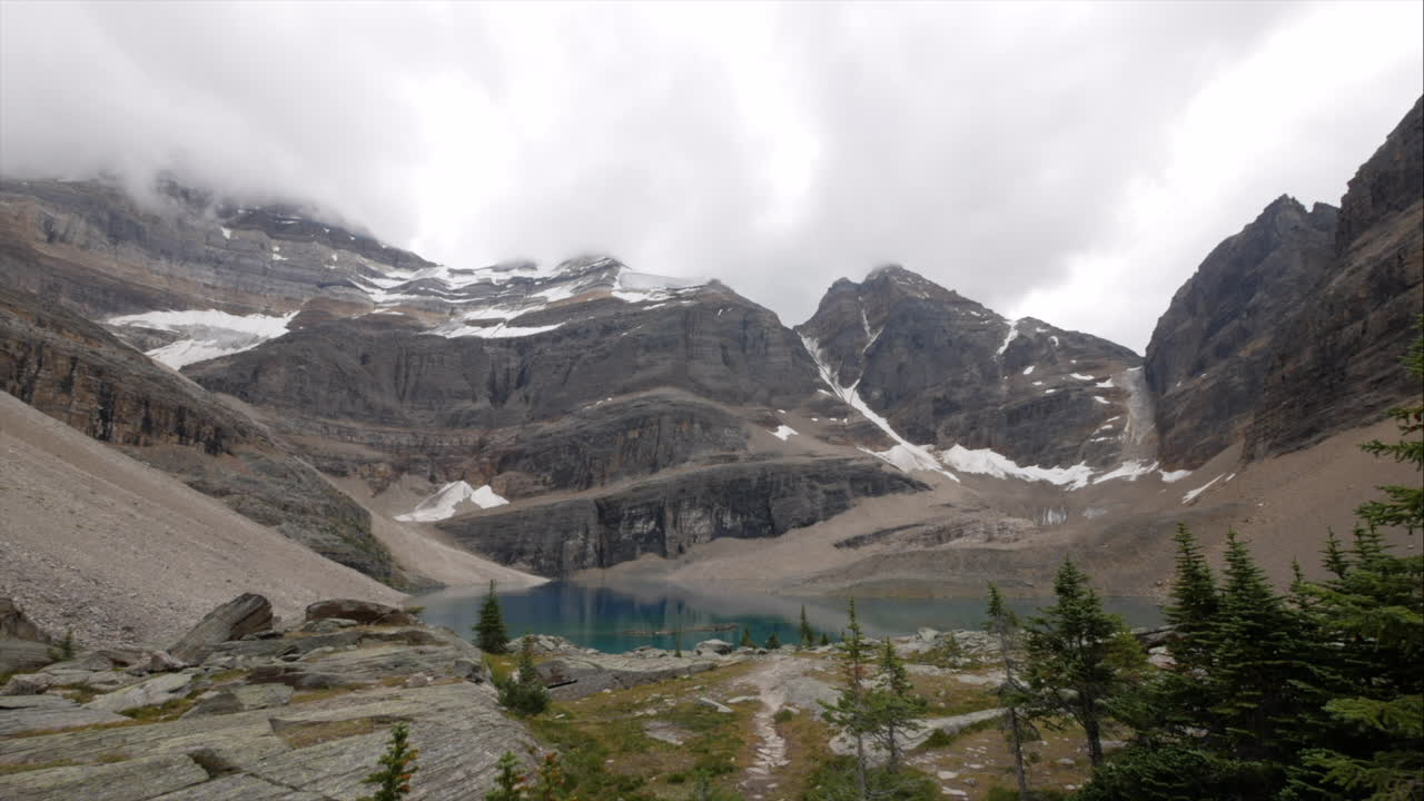 Billowing clouds swirling over snow covered peaks above turquoise waters of Lake O'Hara, Alberta, Canada.