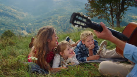 man playing guitar picnic for wife kids close up. happy family listening music.