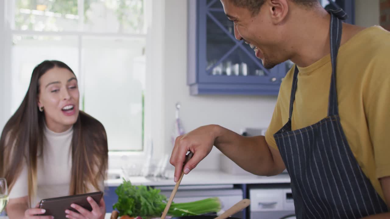 feliz pareja biracial cocinando juntos y riendo en la cocina