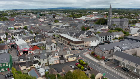 Panoramaaufnahmen-Aus-Der-Luft-Von-Gebäuden-Im-Stadtzentrum.-Kippen-Sie-Nach-Unten-Und-Konzentrieren-Sie-Sich-Auf-Autos,-Die-Eine-Straßenkreuzung-Passieren.-Ennis,-Irland