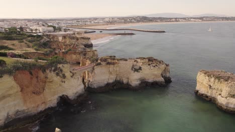 Stone-arch-bridge-at-Praia-dos-Estudantes-against-Lagos-cityscape,-Algarve