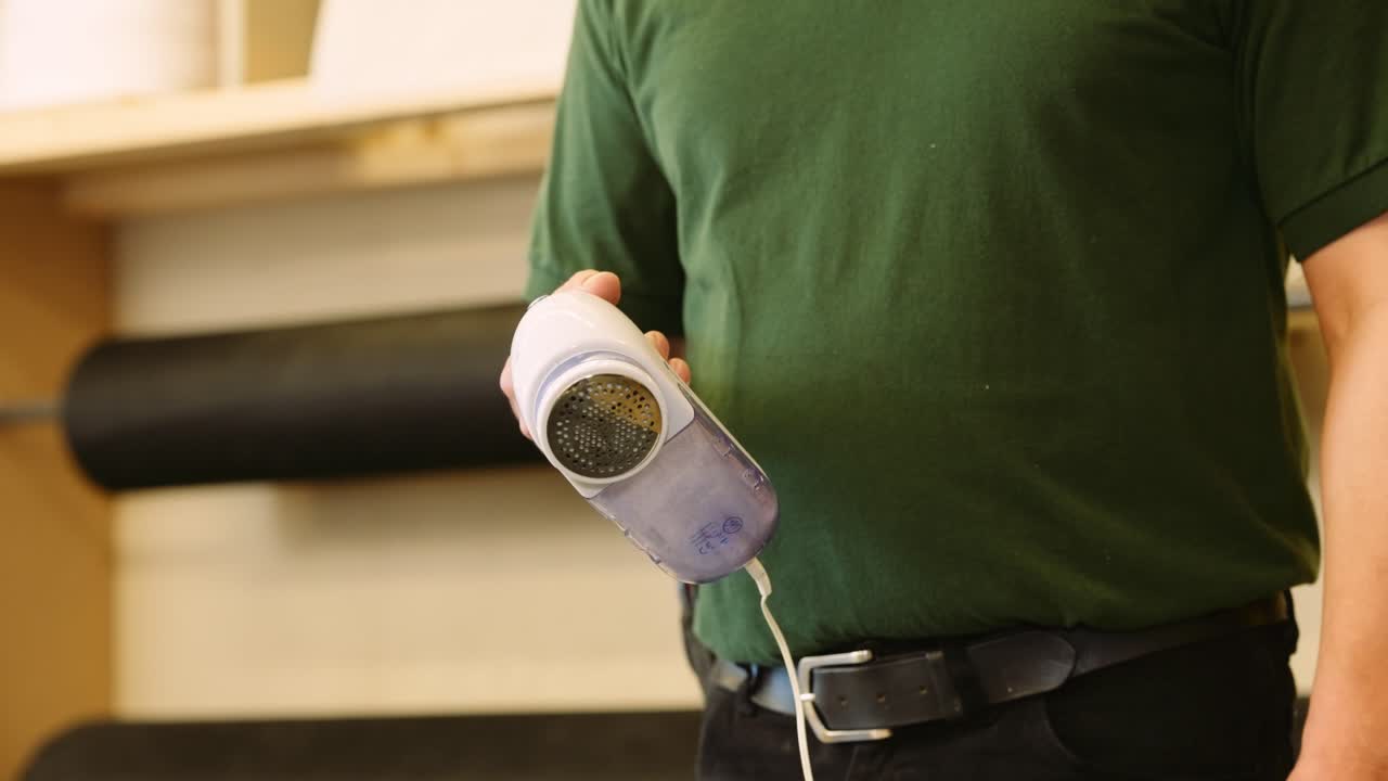 un carpintero de reparación de muebles muestra cómo vaciar la trampa de pelusa en una afeitadora de telas eléctrica