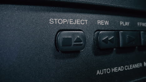 close-up, macro shot of a finger pressing the 'stop' button on a vintage vcr player's control panel