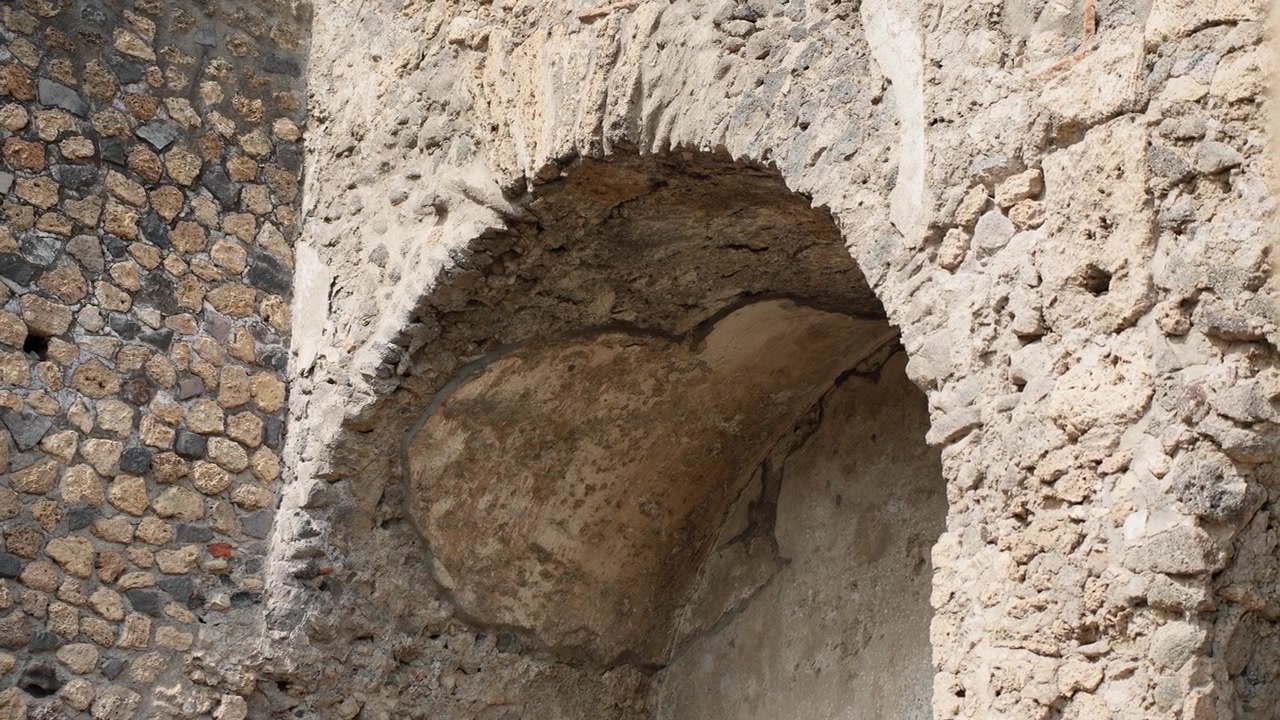 Dettaglio architettonico ravvicinato di una nicchia romana a volta a Pompei, che evidenzia l'intonaco screpolato, la forma curva e l'antica costruzione all'interno delle rovine archeologiche.