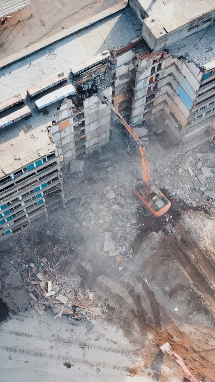 Aerial View Excavators Dismantle The Concrete Structures Of The Building. Powerful claw of excavator demolishing the ruined building. Vertical video