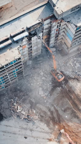 aerial view excavators dismantle the concrete structures of the building. powerful claw of excavator demolishing the ruined building. vertical video