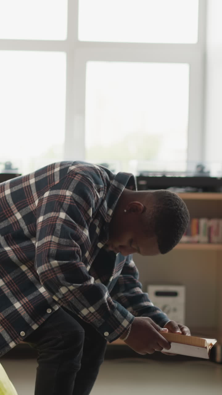un hombre se sienta en una bolsa de frijoles en la biblioteca de la universidad. un estudiante afroamericano disfruta leyendo con comodidad en una moderna librería. educación y pasatiempo