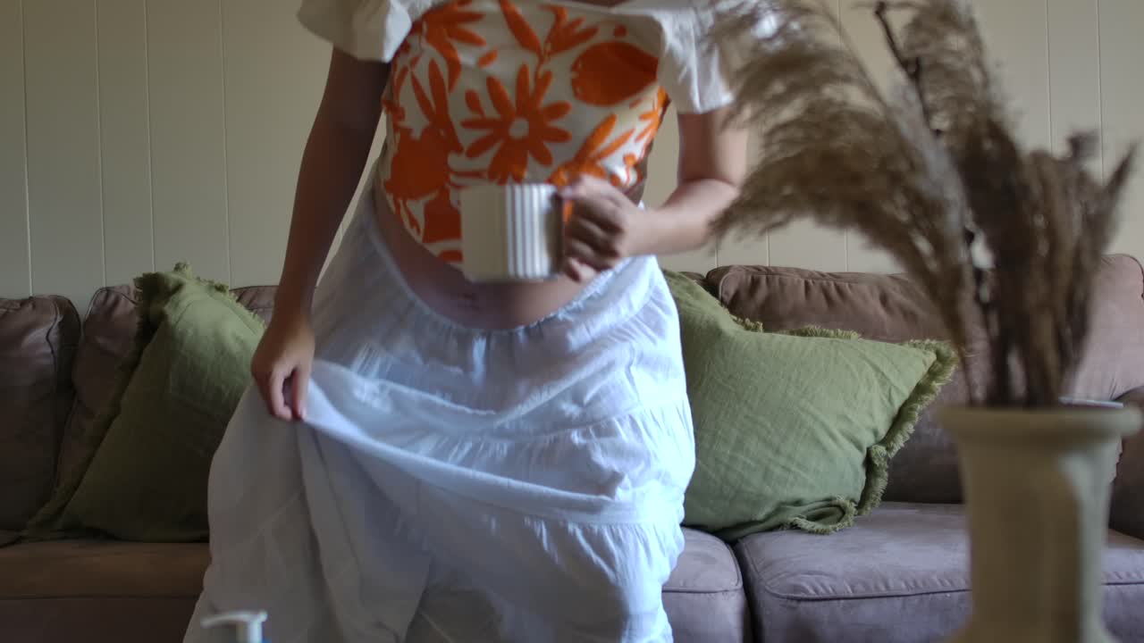 Pregnant Woman with Bare Baby Bumb Belly sits in Sofa with Cup of Tea