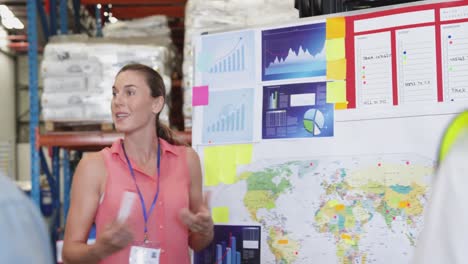 Female-warehouse-manager-in-discussion-with-colleagues-at-an-information-board-4k