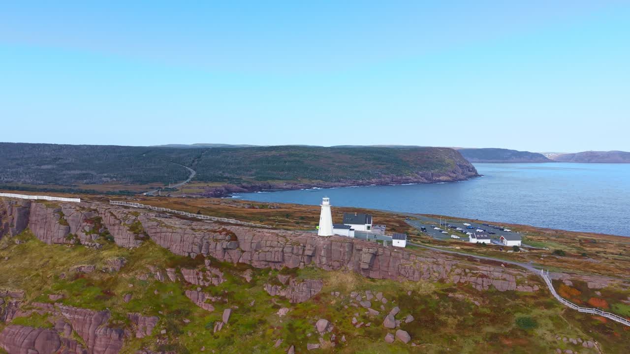 A drone glides over Cape Spear's rugged headland and crashing waves with the historic lighthouse and Signal Hill visible in the distance, filmed outside the national park border