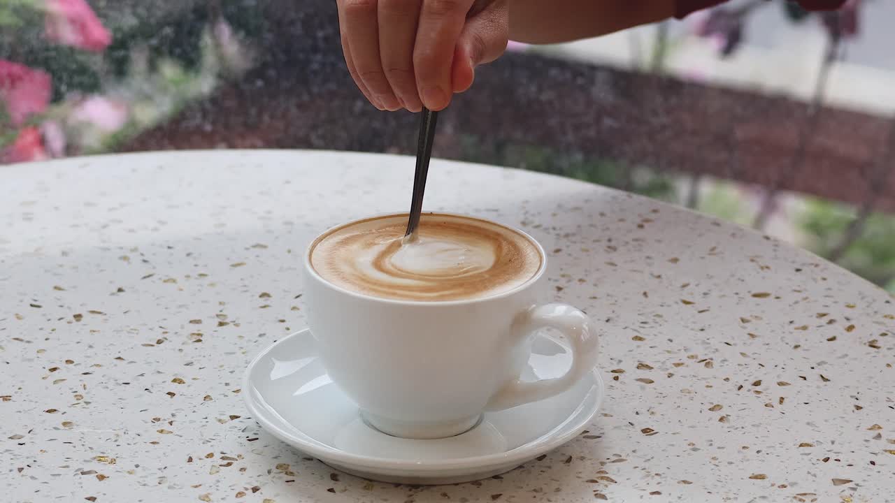 Hand stirring coffee at a cafe table