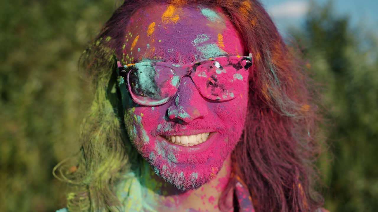 Close-up portrait of joyful bearded man smiling standing outdoors with face covered with paint enjoying Holi festival