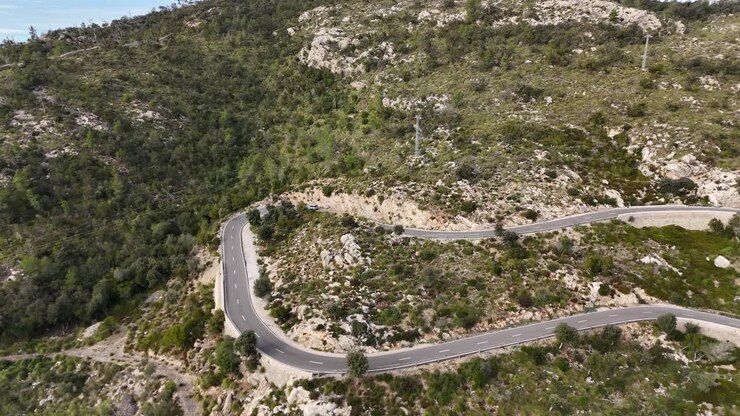 Ripresa aerea di un'auto su una strada tortuosa sulle montagne di Maiorca in una giornata di sole - Strada per la città di Esporles