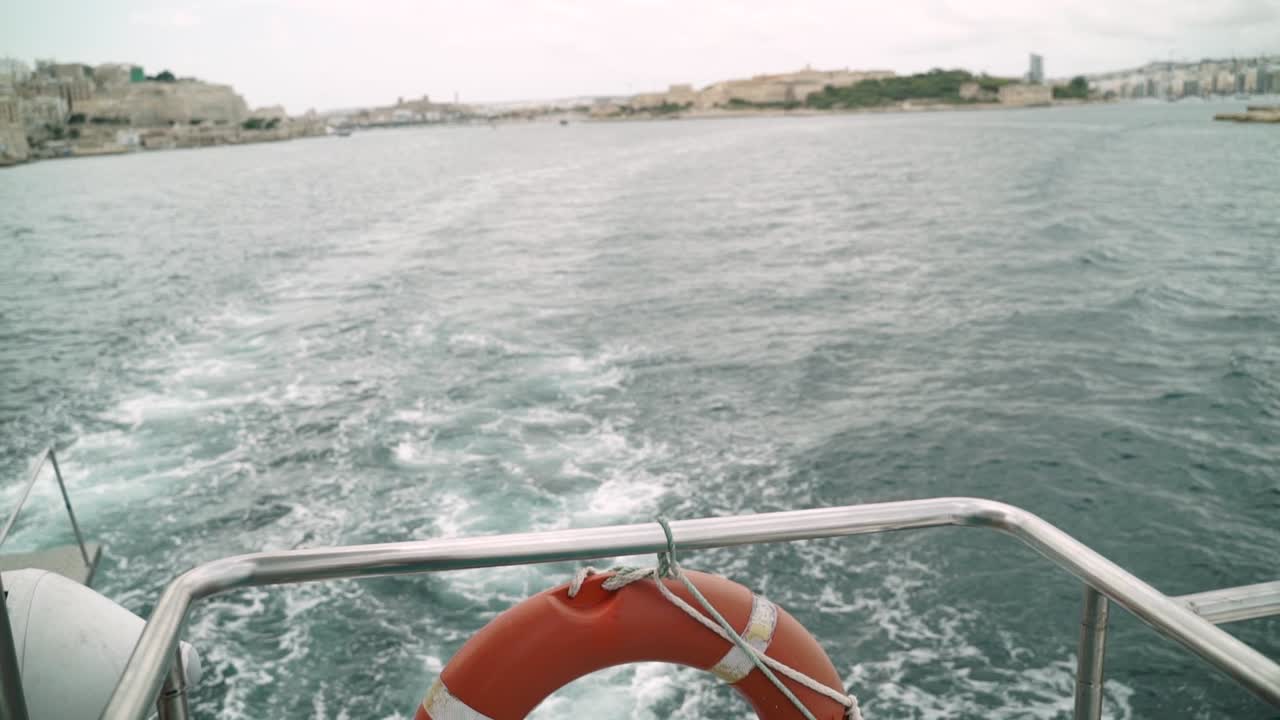 Inquadratura dal basso verso l'alto dalla poppa di una barca in movimento verso la città vecchia di La Valletta, Malta, in lontananza